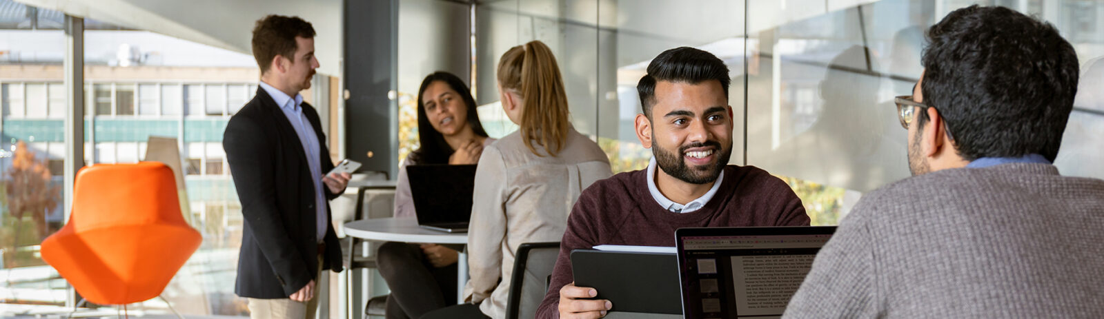 People in business attire sit at hightop tables working on laptops.