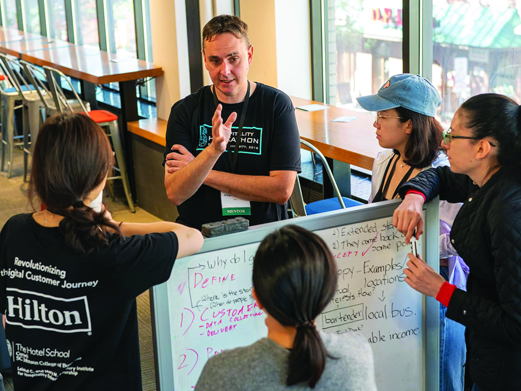 A mentor stands around a whiteboard with four students.