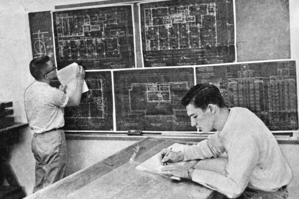 A black and white photo of two men writing on papers.